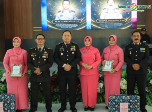 "Enam peserta acara, terdiri dari personel kepolisian dan anggota Bhayangkari, berpose bersama dalam acara seremonial resmi di dalam ruangan dengan logo Warta Edukasi di pojok kanan atas."